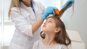 Lice technician using an orange nit comb on a child's sectioned hair during a professional mayo for lice comb-out
