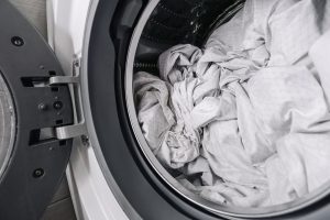 Open front-loading washing machine drum filled with white bed sheets ready for a hot wash cycle after a lice diagnosis