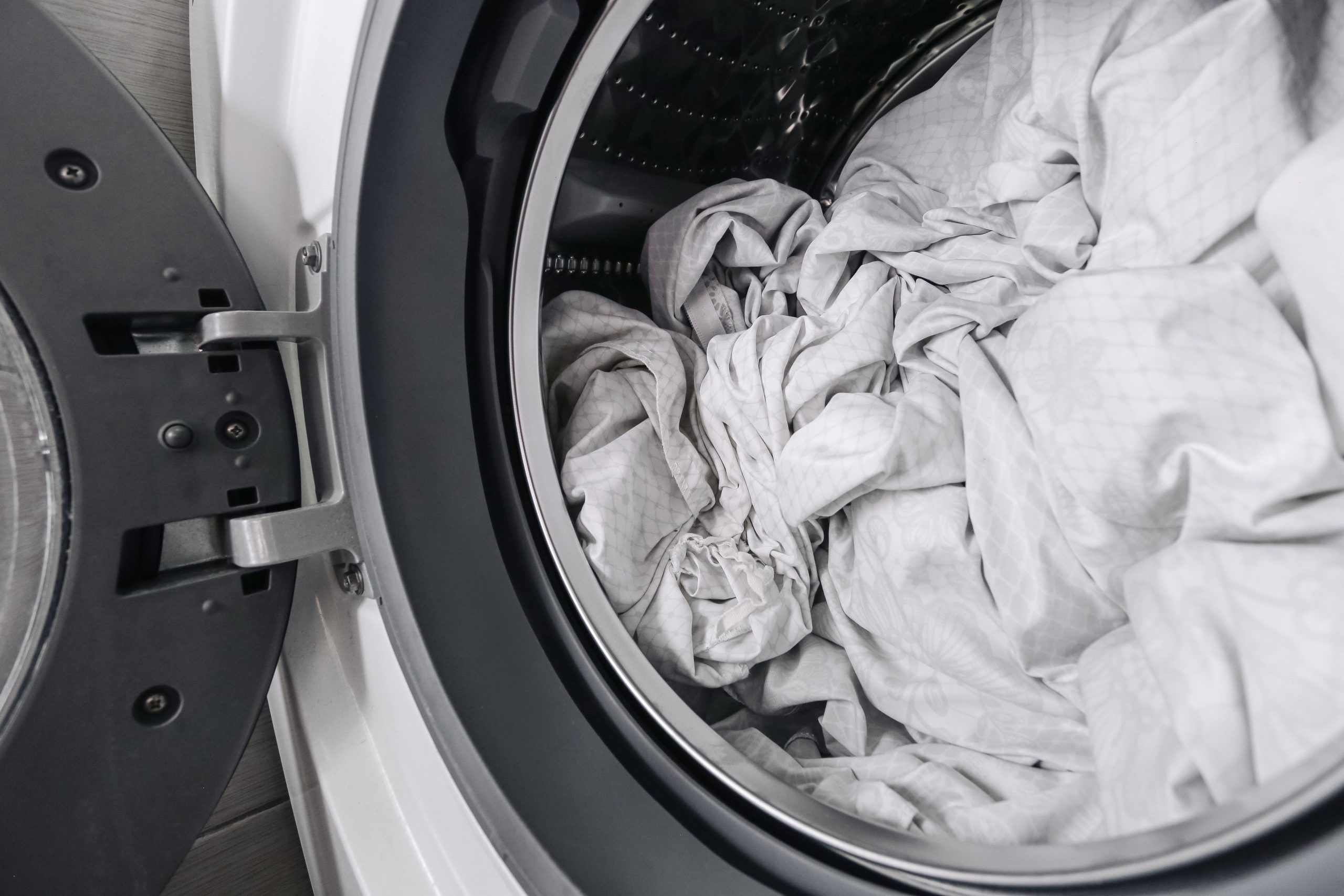 Open front-loading washing machine drum filled with white bed sheets ready for a hot wash cycle after a lice diagnosis