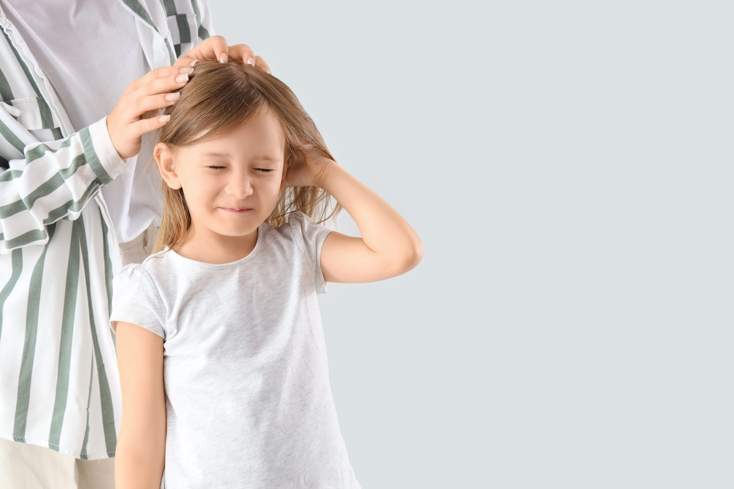 A parent gently parting and inspecting a young child's clean hair under bright light to check for head lice and nits at home.