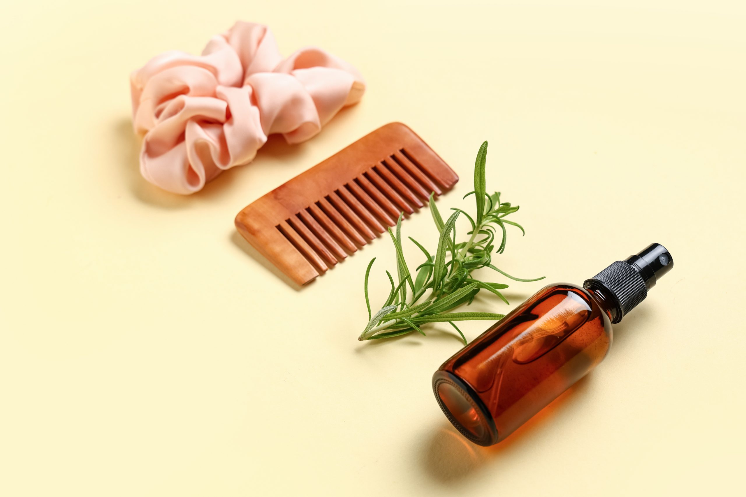 Wooden hair comb, fresh rosemary sprig, and amber glass spray bottle resting on a soft surface — the natural daily-prevention spray essentials parents consider for head lice