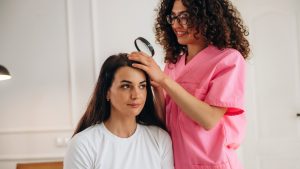 Mother using a handheld magnifying glass to check her young daughter's scalp for head lice at the kitchen table in natural light