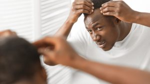 African American mom gently brushing her young daughter's curly hair while checking the scalp at home in soft natural light