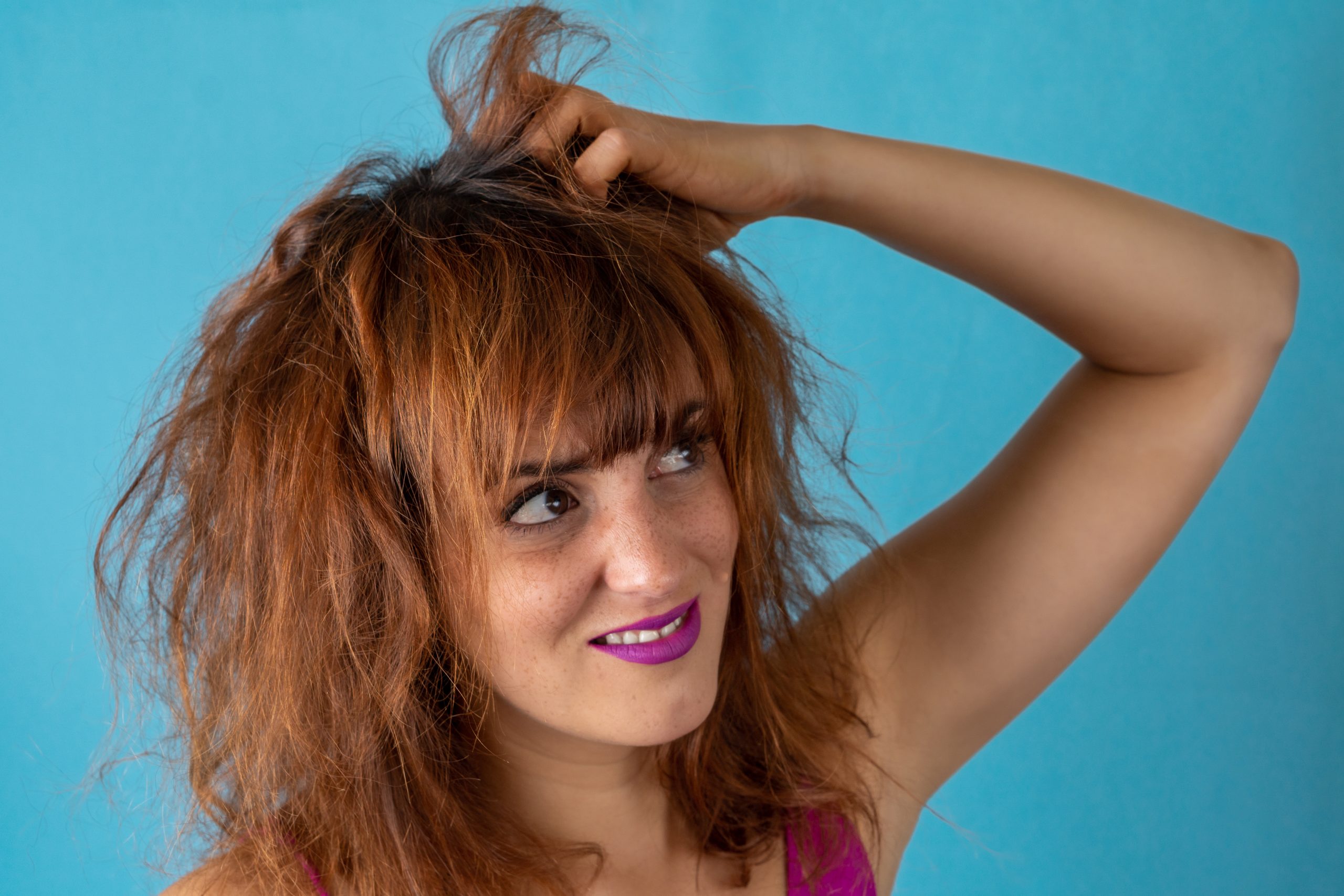 Worried young woman with tousled red hair scratching her head