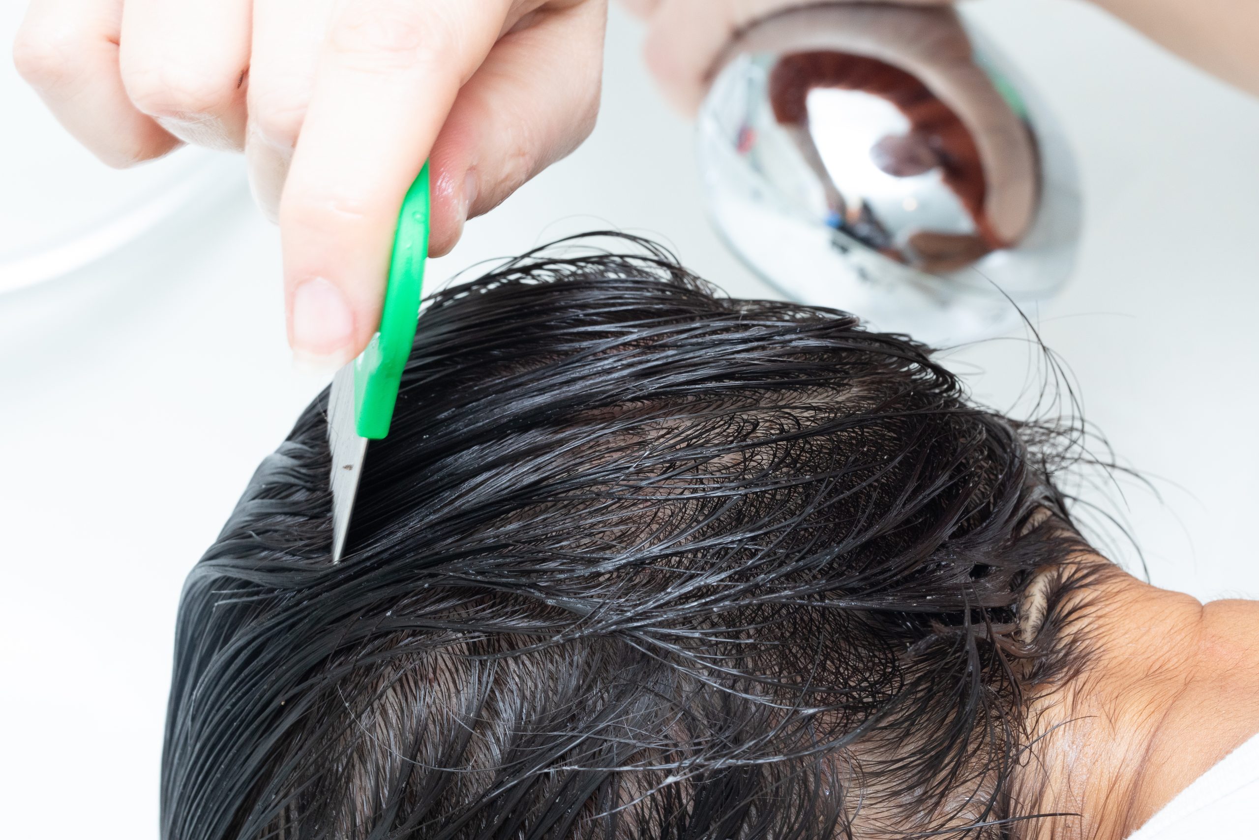 Parent running a fine-tooth lice comb through a child's wet hair to confirm the scalp is clear of lice and nits