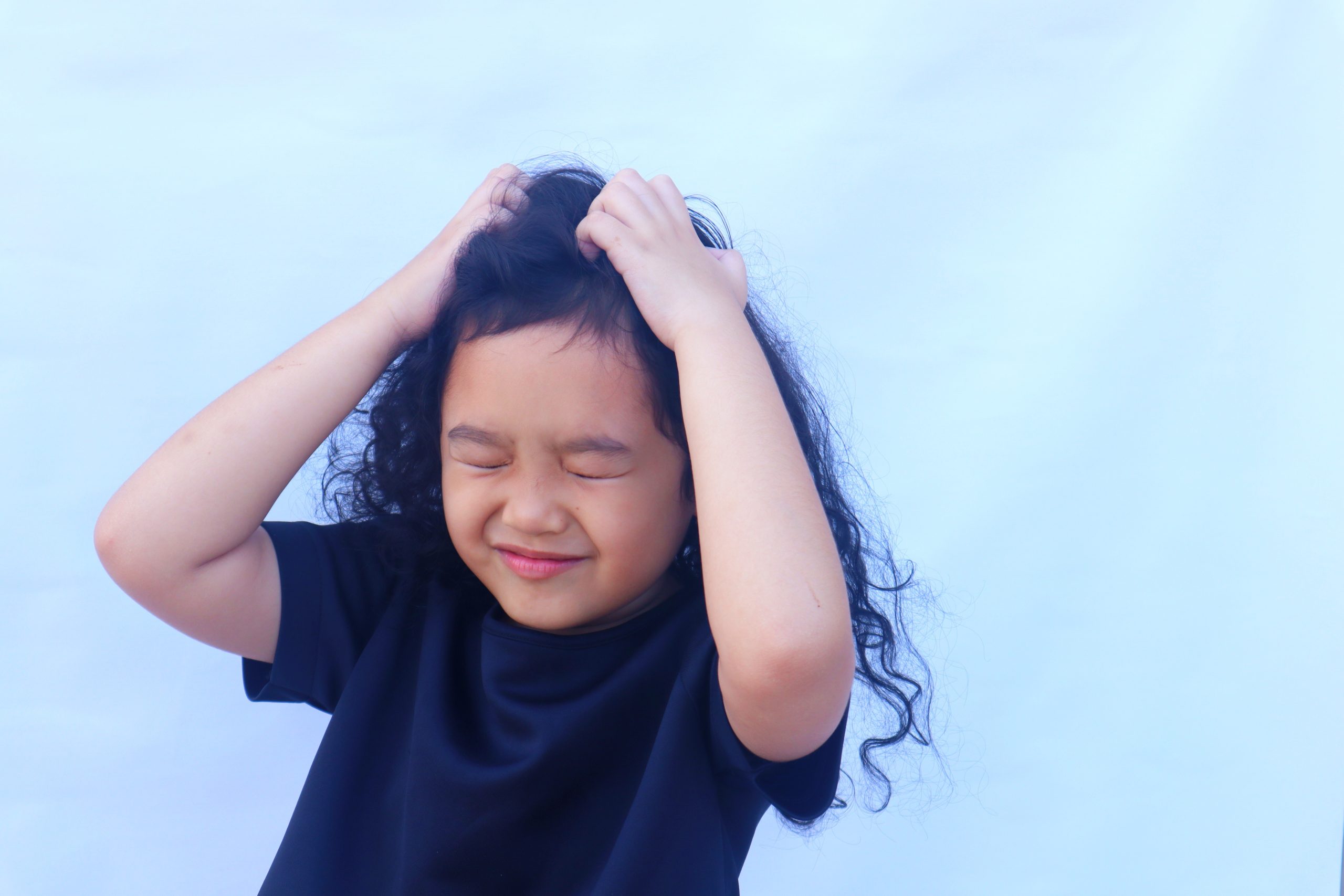 A child scratches an itchy scalp, the delayed allergic reaction to head lice that can lag weeks behind the infestation.