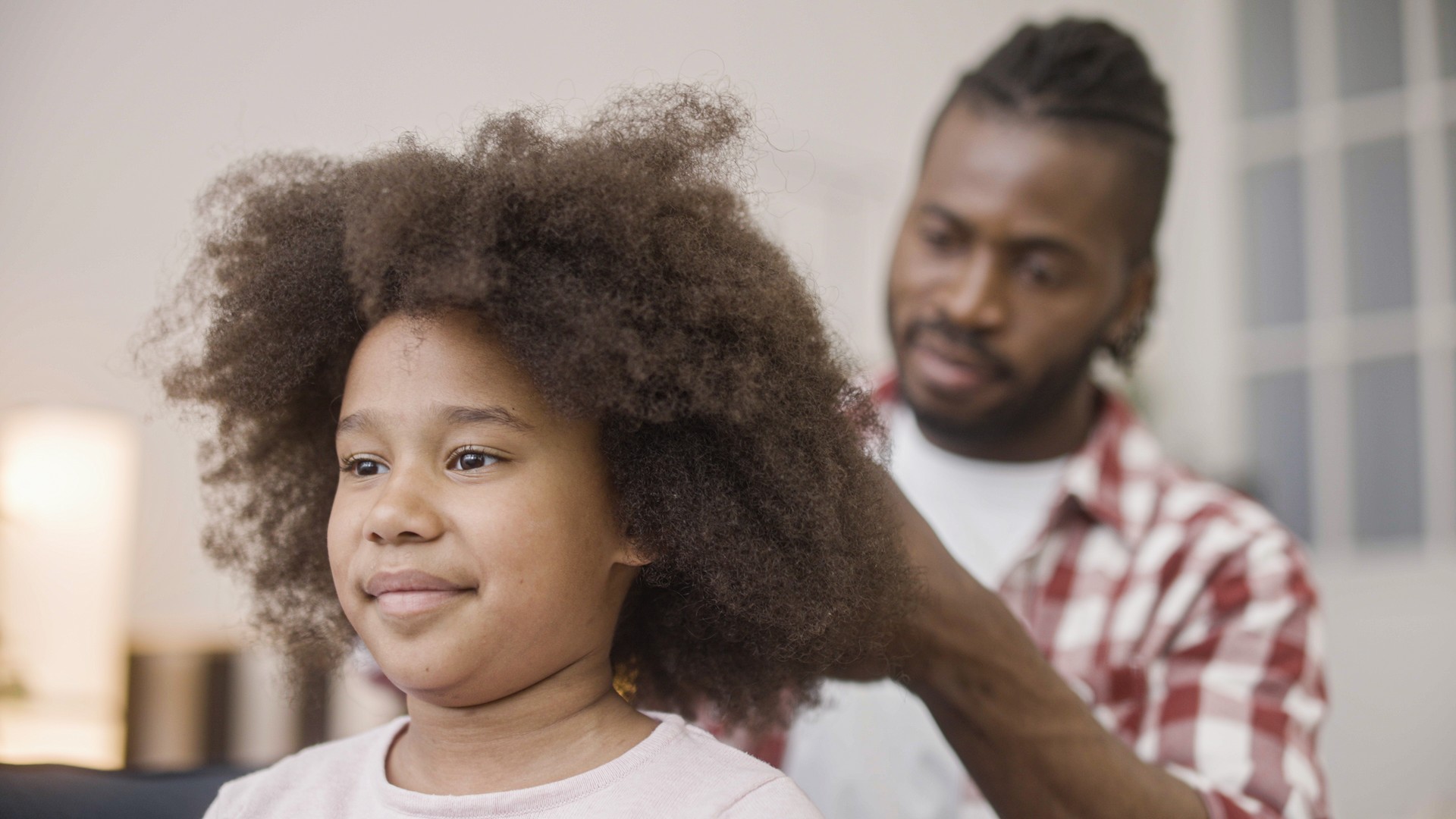 A parent draws a fine-tooth comb through a child's natural textured hair, the hands-on comb-out that removes lice and nits a relaxer cannot.