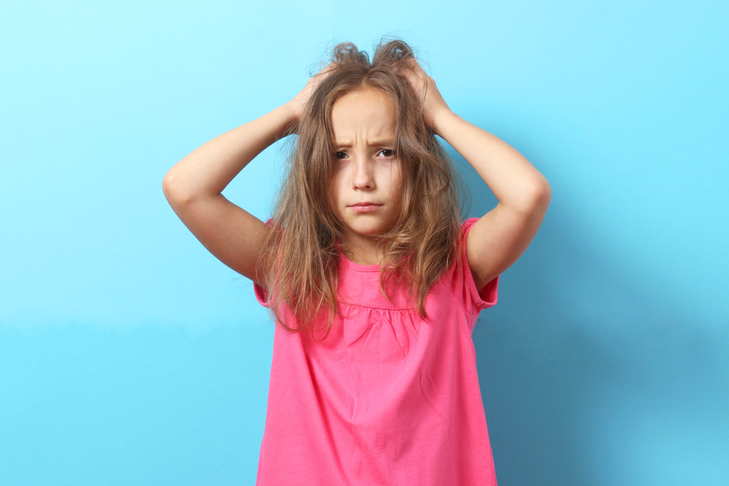 A young girl scratches her itchy head while a parent wonders whether it is head lice or scabies
