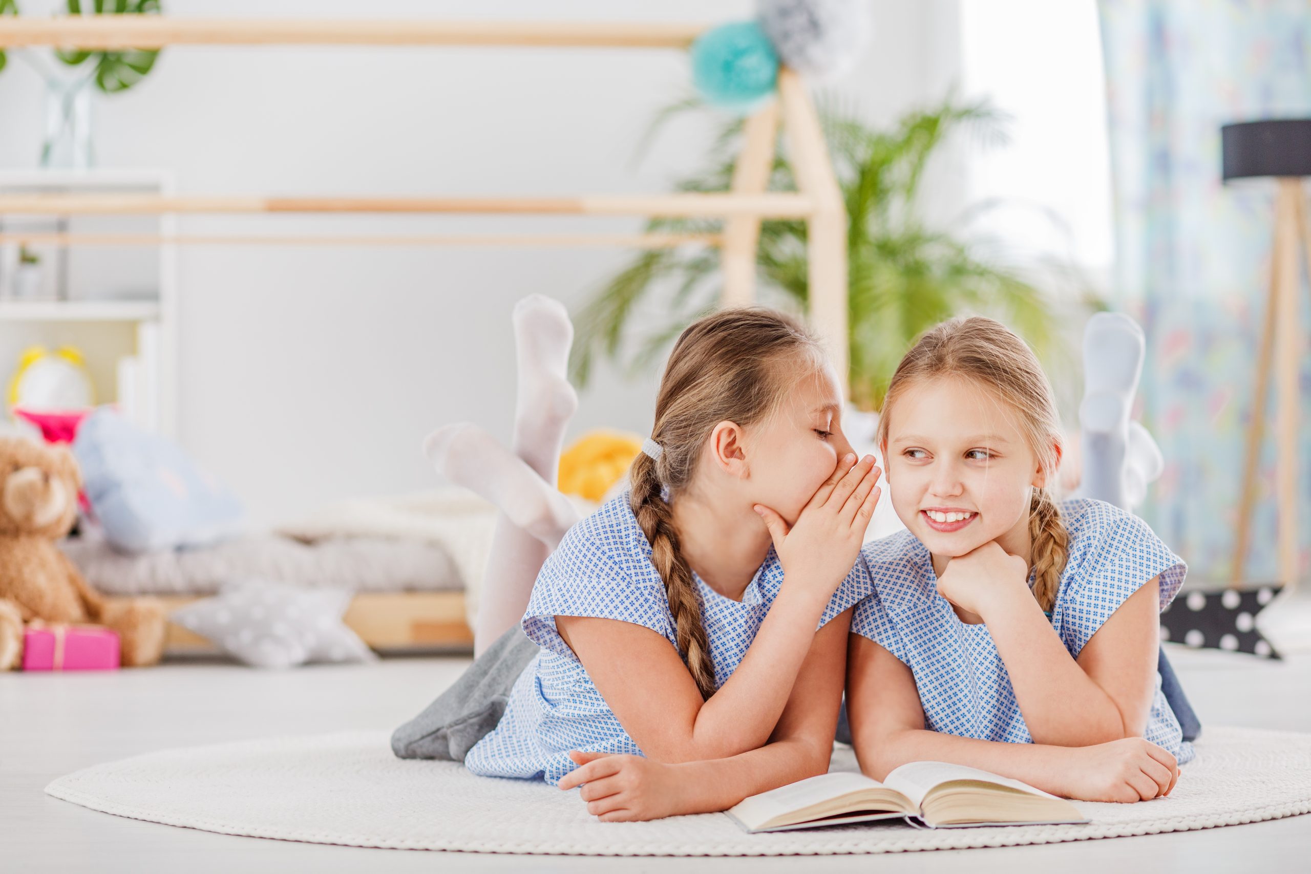 Children whispering close together to illustrate how lice spreads through close contact